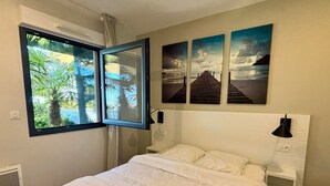 Une chambre à coucher avec un lit, une fenêtre donnant sur des palmiers et trois tableaux accrochés au mur.