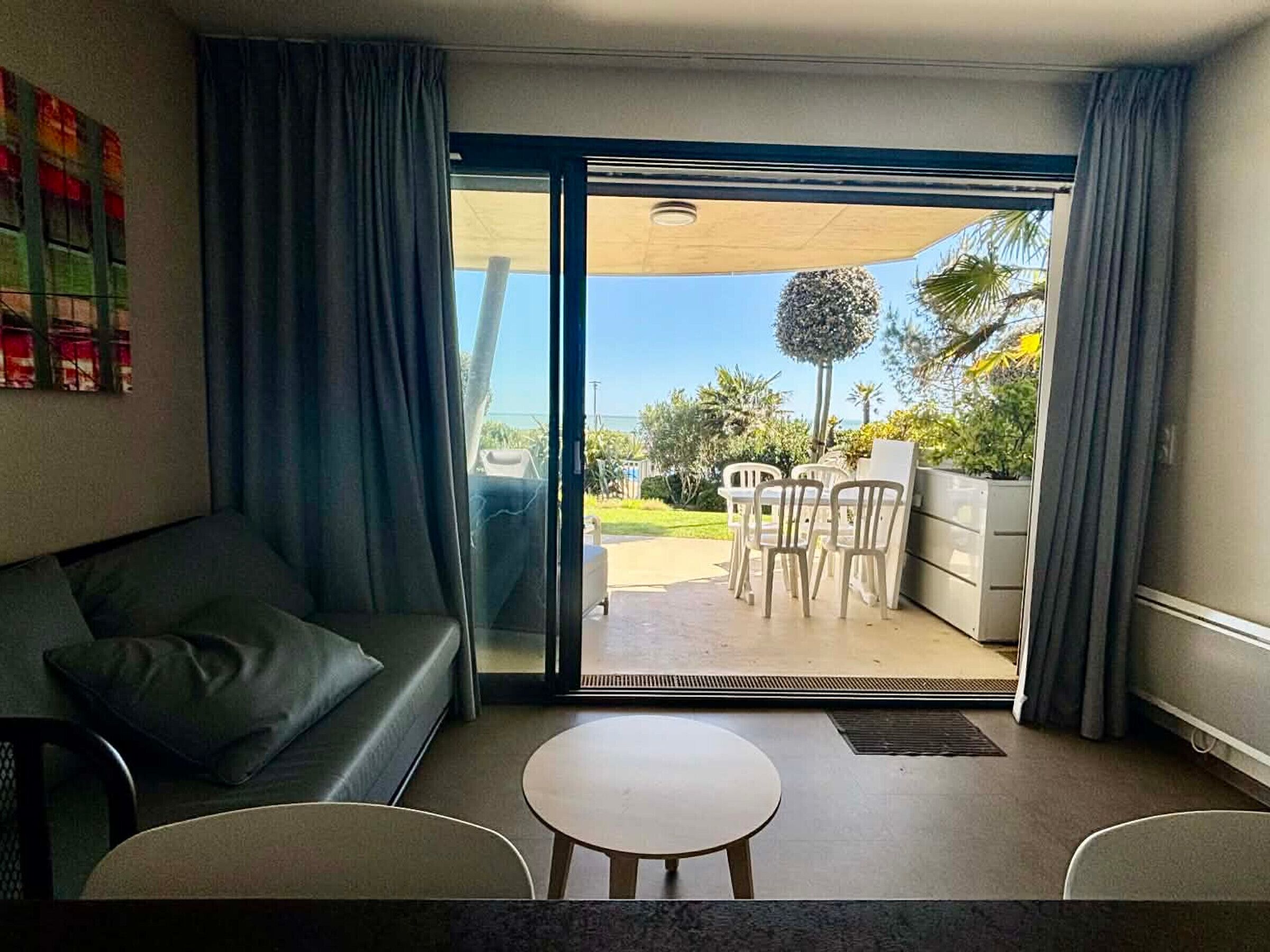 A living room with a sofa, a small round table, and a sliding glass door leading to an outdoor patio with a table and chairs.