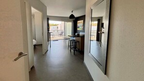A hallway leading to a balcony with a dining area, a TV, and a painting on the wall. - Coastal Apartment, 2BR, Balcony, Pool, Beach Access, PMR Friendly, Pets Welcome, La Tranche-sur-Mer (La Tranche-sur-Mer)