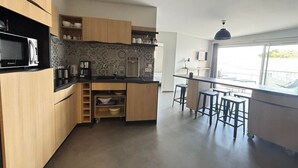 A modern kitchen with wooden cabinets, a built-in microwave, and a small island with stools. - Coastal Apartment, 2BR, Balcony, Pool, Beach Access, PMR Friendly, Pets Welcome, La Tranche-sur-Mer (La Tranche-sur-Mer)
