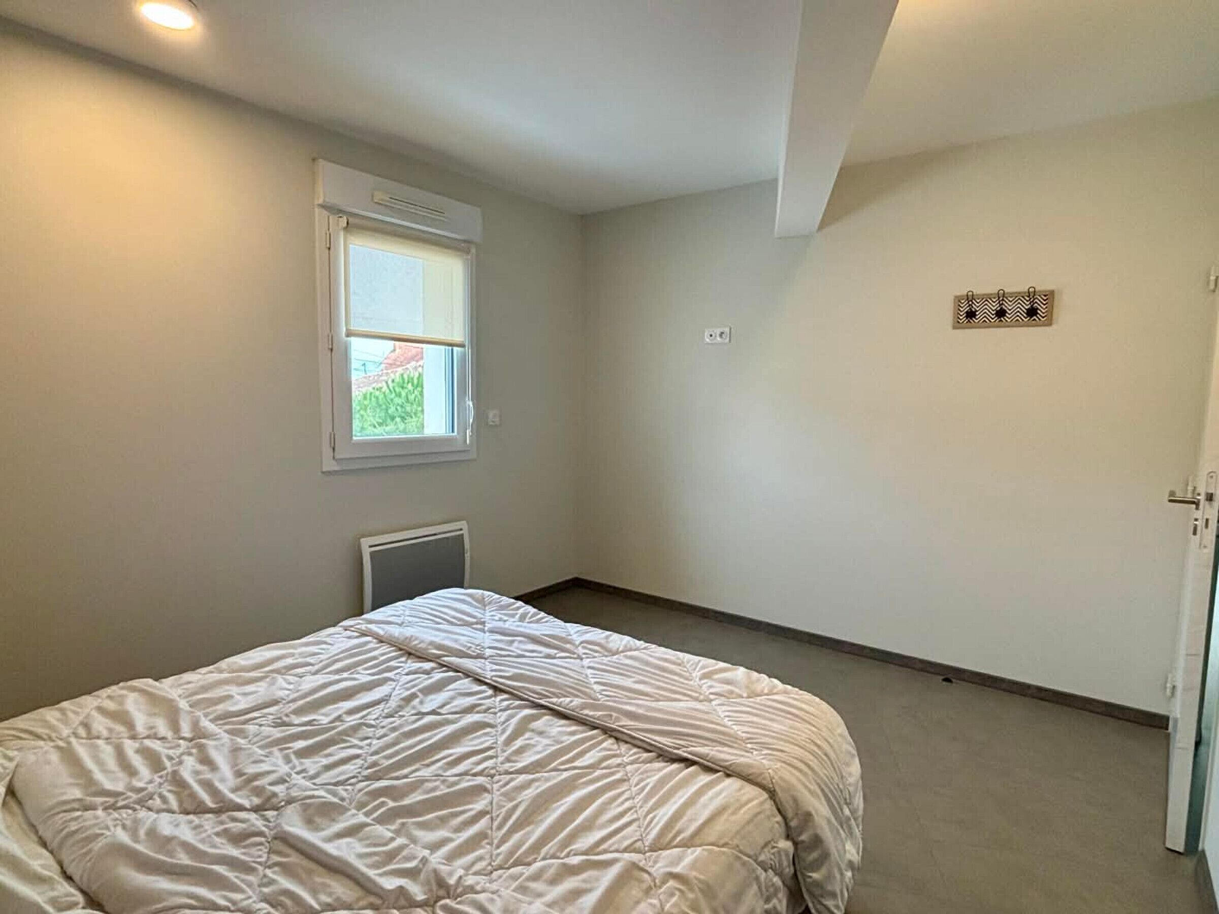 A bedroom with a bed, a window, a radiator, and a door.