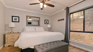 A bedroom with a bed, bedside lamps, a ceiling fan, a large window, and a view of the outdoors. - Mammoth Condo with Hot Tub (Mammoth Lakes)