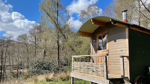 A wooden cabin with a balcony, a chimney, and a small window. - Cosy Woodland off Grid Shepherds Hut - Hazel (Castle Douglas)