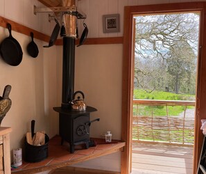 Una habitación acogedora con una estufa de leña, un ventanal con vistas a un paisaje verde y una puerta que da al exterior.