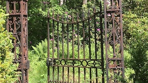 A wrought iron gate with intricate designs, surrounded by lush greenery and trees. - Cosy Woodland off Grid Shepherds Hut - Hazel (Castle Douglas)