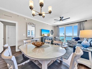 A spacious living room with a round glass table, a chandelier, and a ceiling fan.