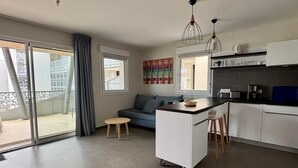 Una cocina moderna con una isla central, un área de comedor con un sofá azul y un ventanal corredero que da a un espacio exterior.