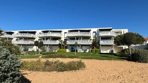 Un edificio moderno con varios balcones, un primer plano de arena y vegetación.