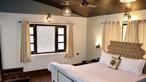Un dormitorio con una cama grande, cabecera de madera y una ventana con cortinas. Hay una mesita de noche con una lámpara y un teléfono.