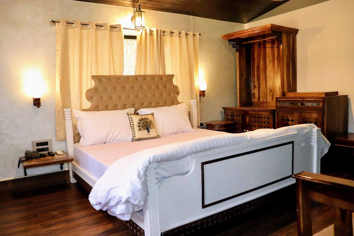 A bedroom with a large bed, wooden headboard, white bedding, and a nightstand with a telephone.