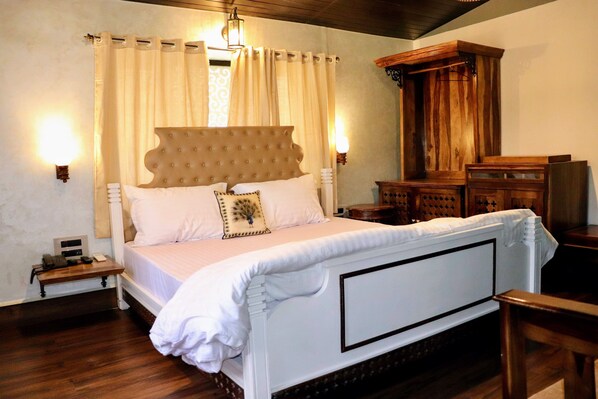 Un dormitorio con una cama grande, cabecera de madera, ropa de cama blanca y una mesita de noche con teléfono.