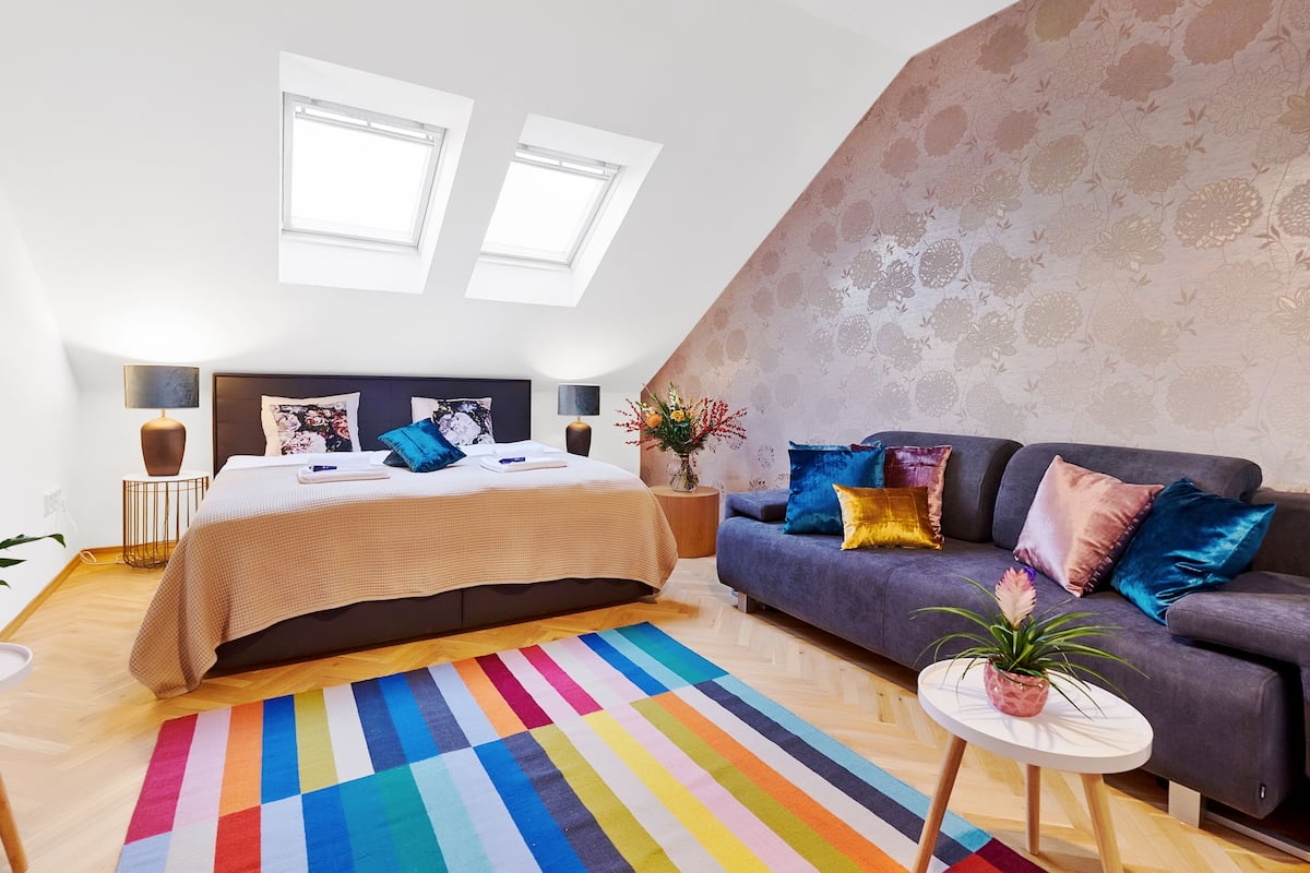 Ein modernes Schlafzimmer mit Bett, Sofa, kleinem Tisch und einer Topfpflanze.