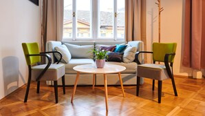A living room with a sofa, two chairs, a small table with a plant, and a window with curtains. - Royal Route Residence Lesser Town (Prague)