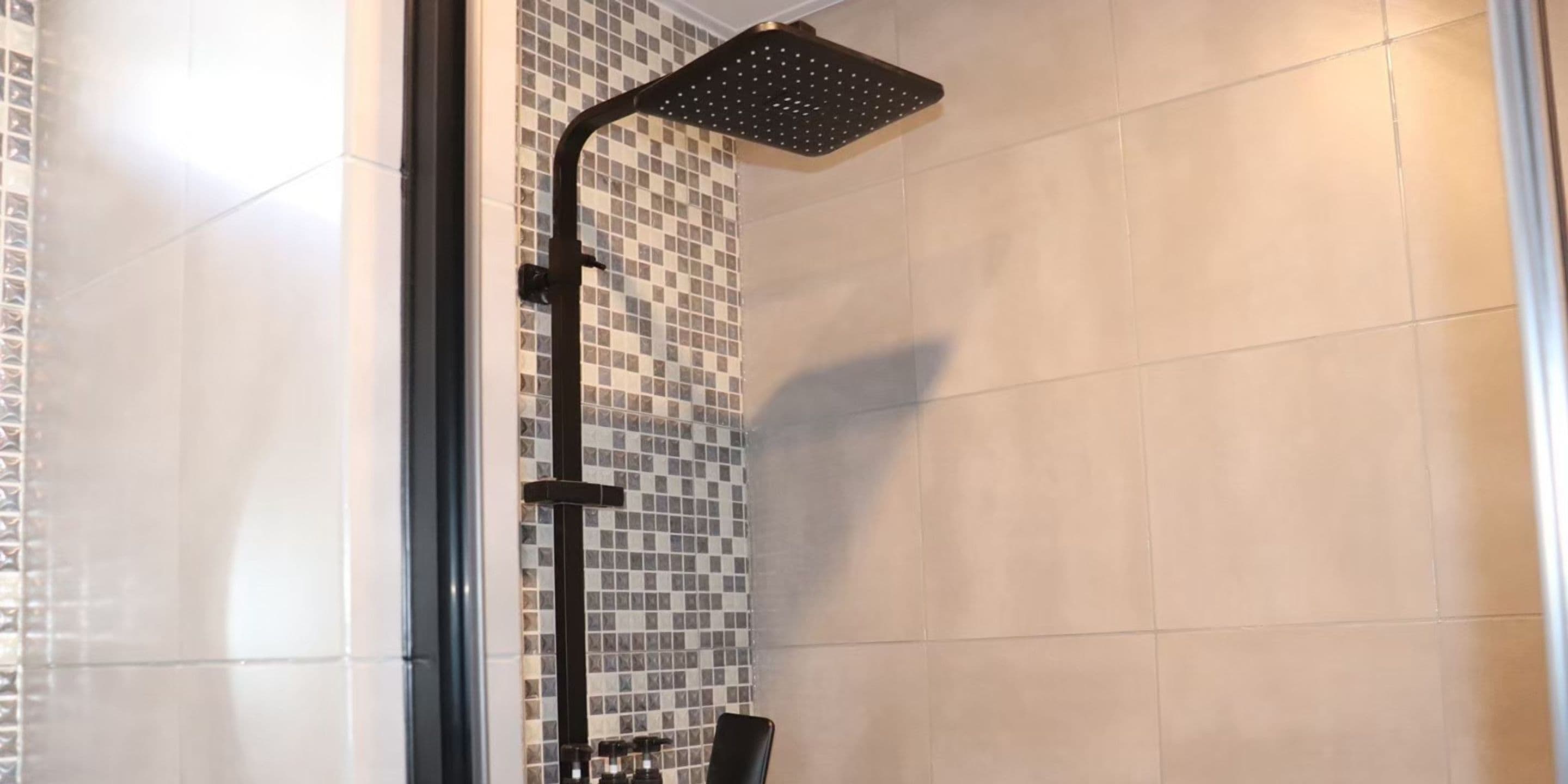 A shower with a black rain shower head, tiled walls, and a glass door.