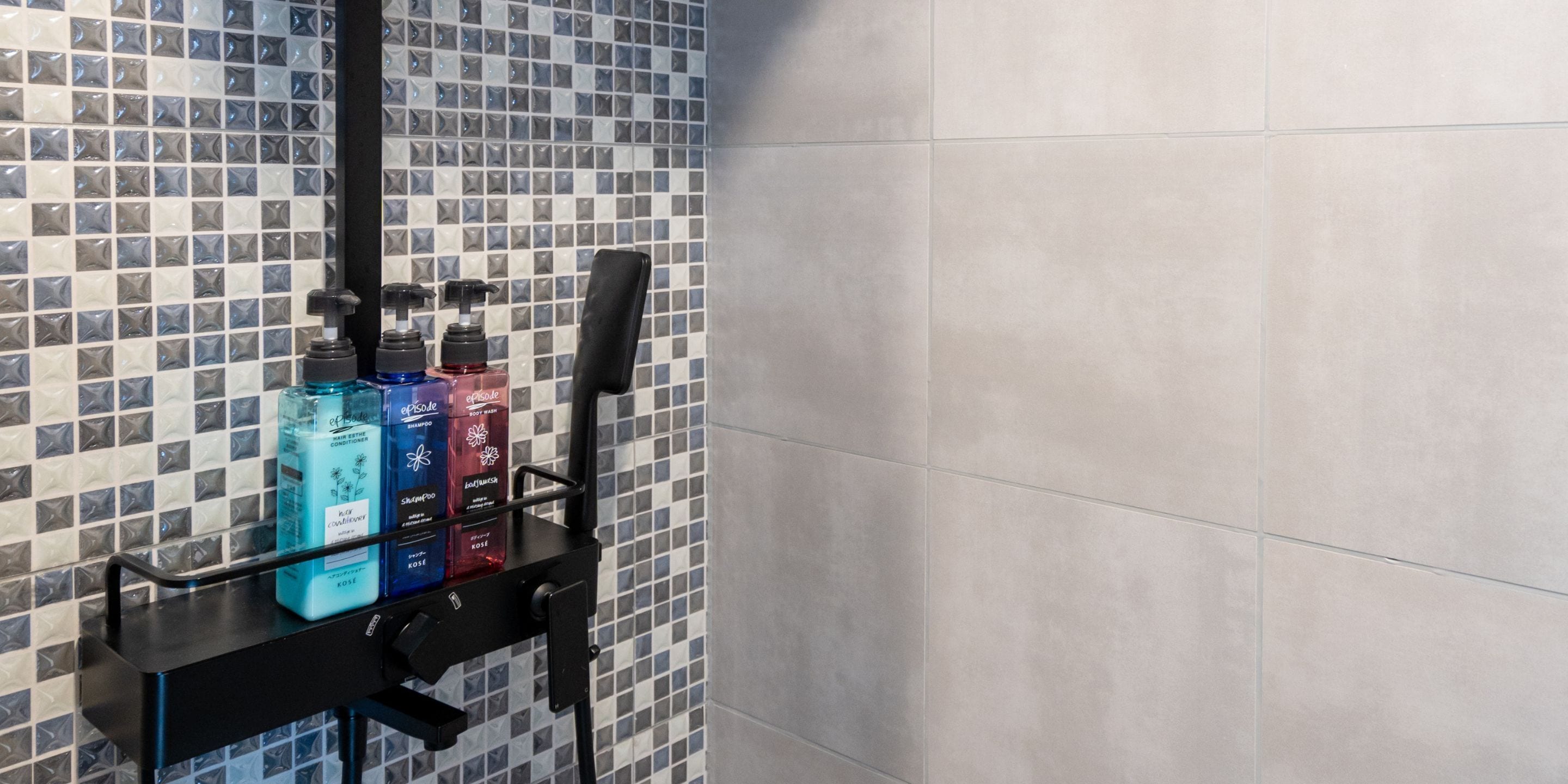 Baño con salpicadero de azulejos y toallero negro que sostiene tres botellas de champú y acondicionador.
