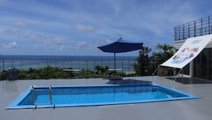 A swimming pool with a view of the ocean, a blue umbrella, and a sign indicating the front of the property.