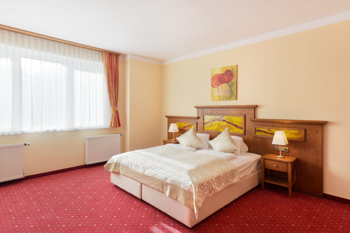 Un cuarto de hotel con una cama grande, dos mesitas de noche, una ventana con cortinas y un cuadro en la pared.