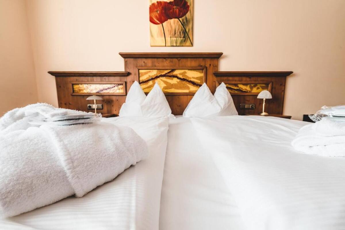 Habitación de hotel con cabecera de madera, dos camas con sábanas blancas, un cuadro de flores rojas y una lámpara en la mesita de noche.