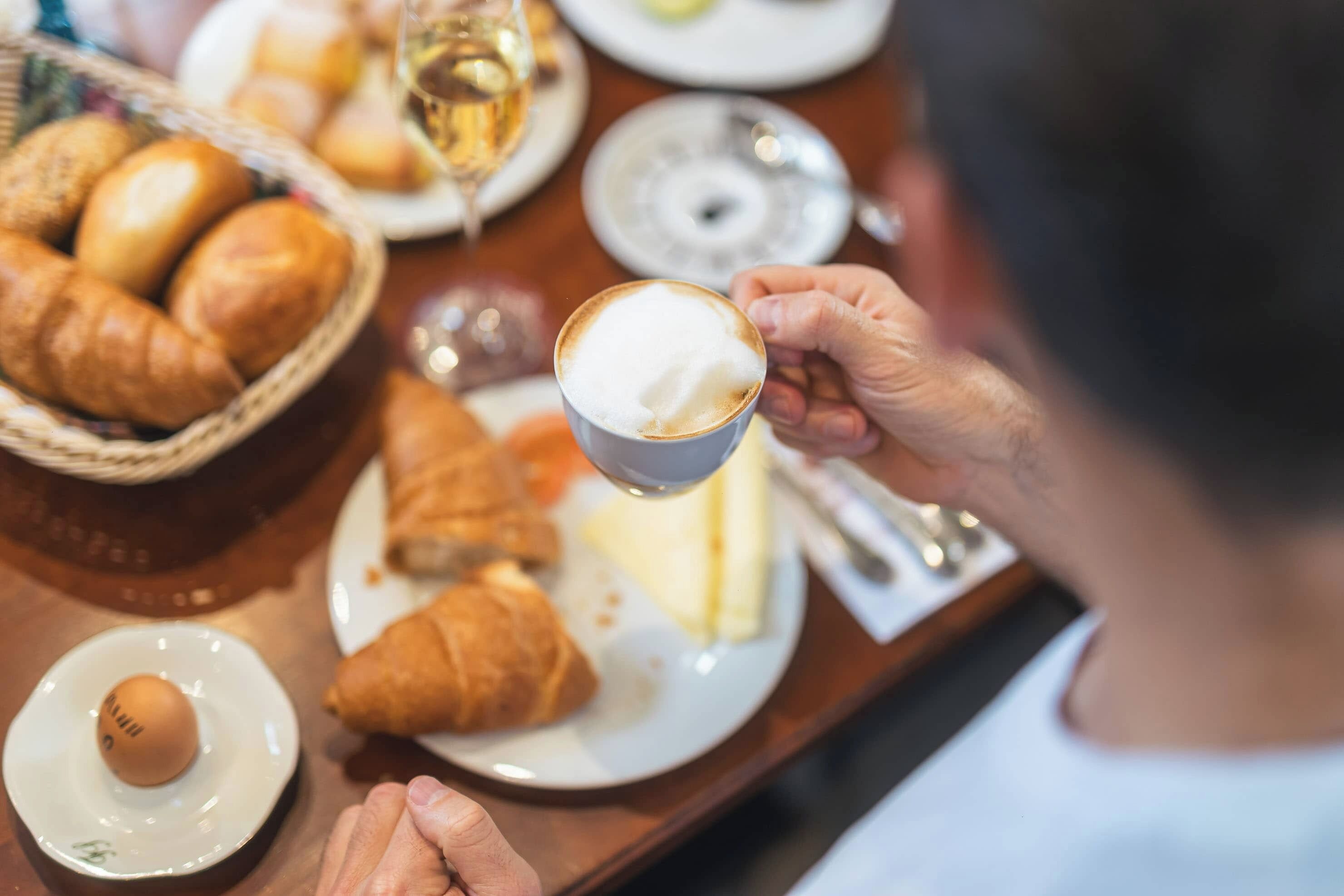 A dining table with croissants, a plate with a croissant half-eaten, a small plate with a single egg, and a cup of coffee.