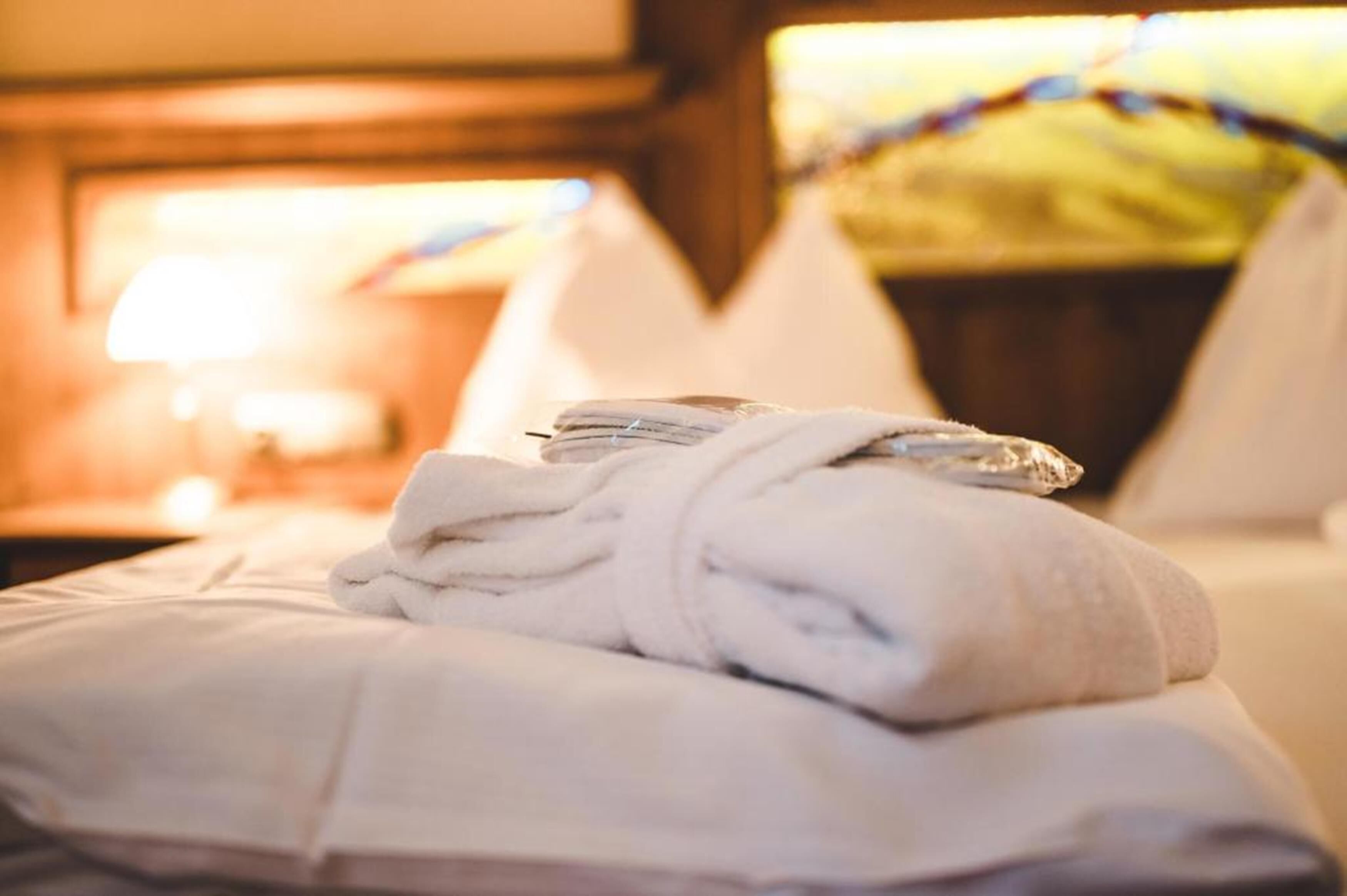 A neatly made bed with a folded white towel and a rolled-up towel on top.