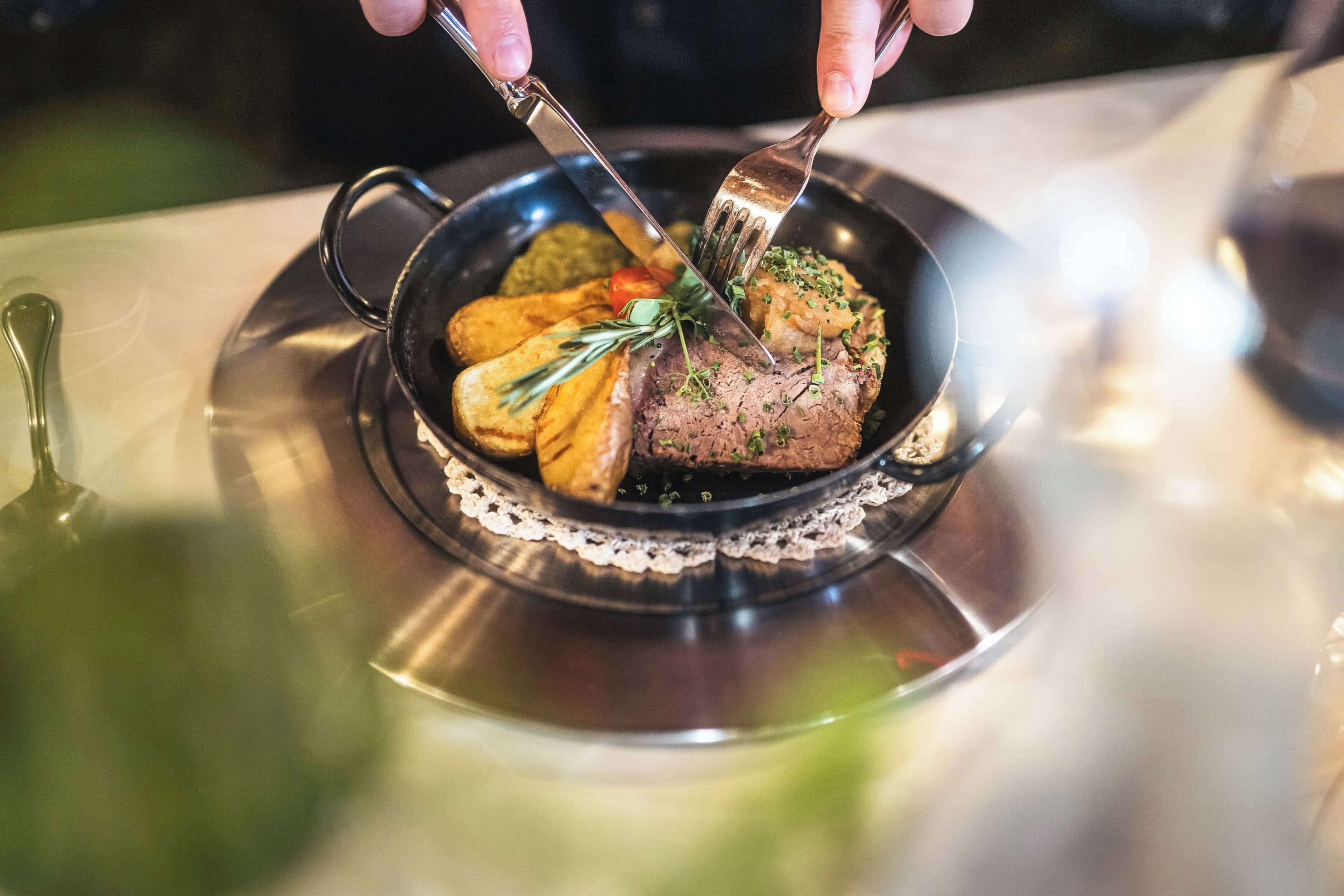 A dish with steak, vegetables, and a garnish on a black plate with a lace doily.
