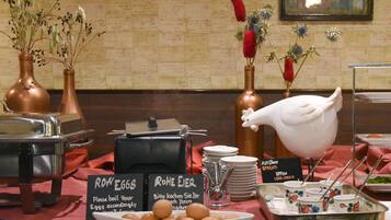 A breakfast buffet setup with labeled dishes, including eggs and cheese, and decorative vases with flowers.