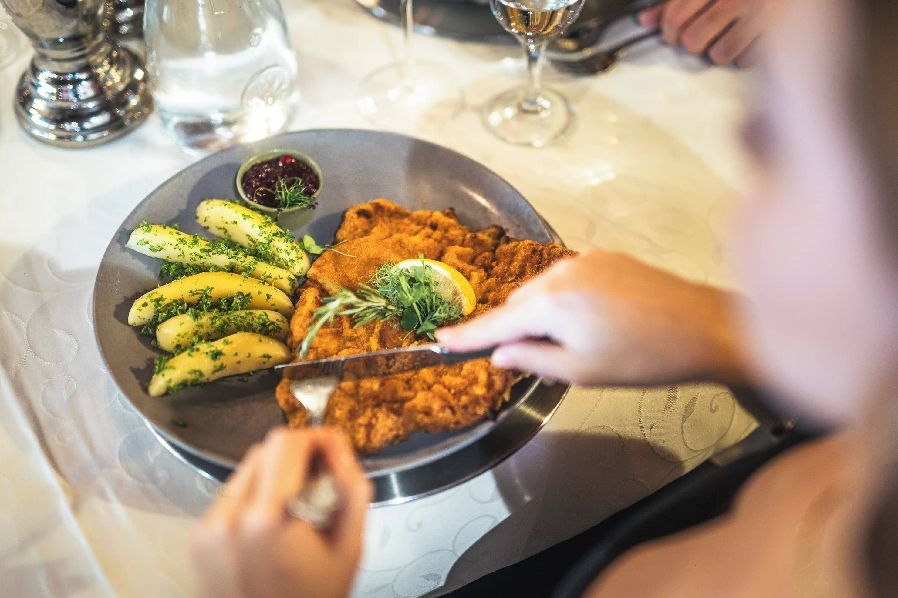 A person cutting a piece of breaded meat with a knife.