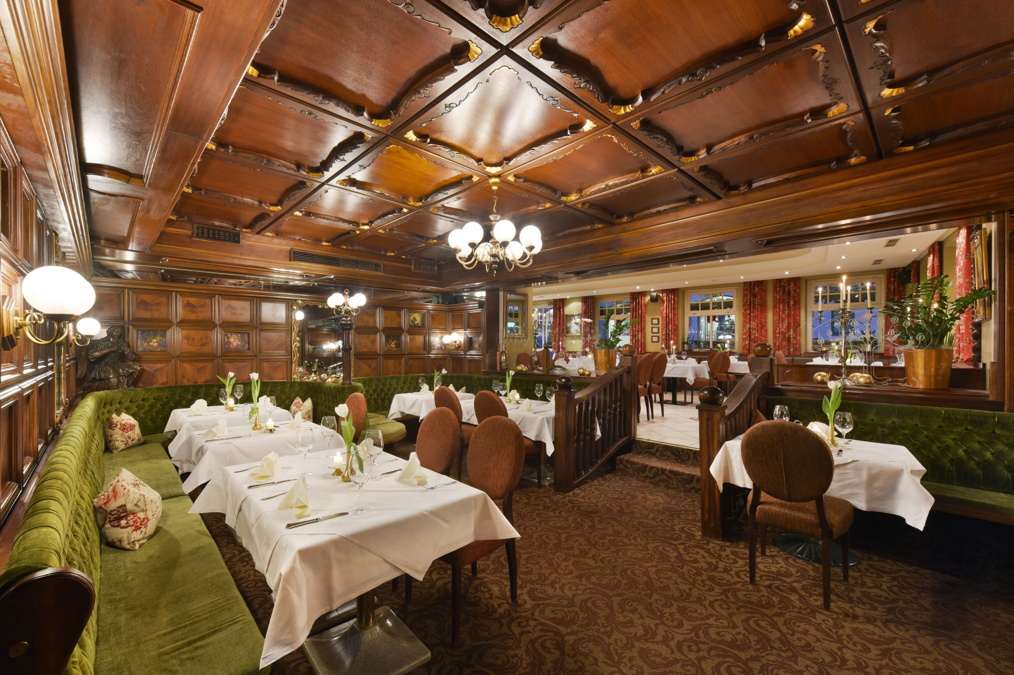 Una sala da pranzo formale con diversi tavoli apparecchiati, una panca imbottita verde e un lampadario.