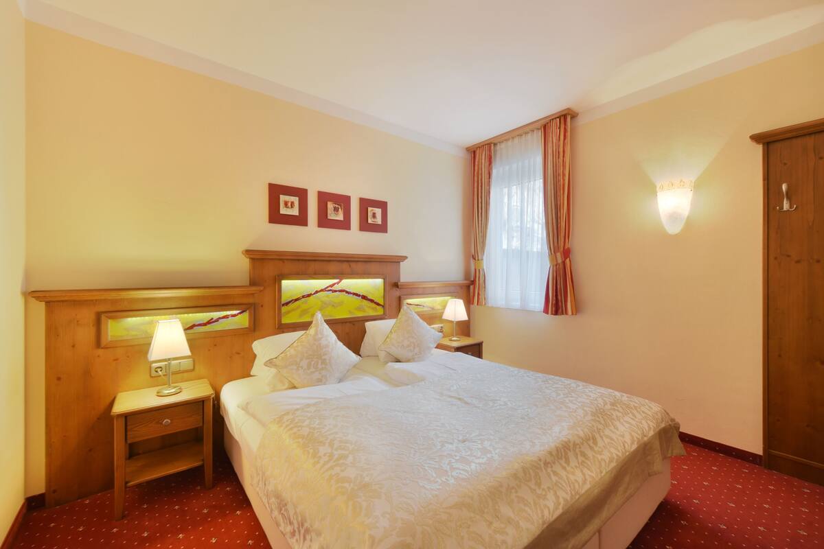 Habitación de hotel con cama, mesitas de noche, lámpara de pared, un cuadro y un armario.