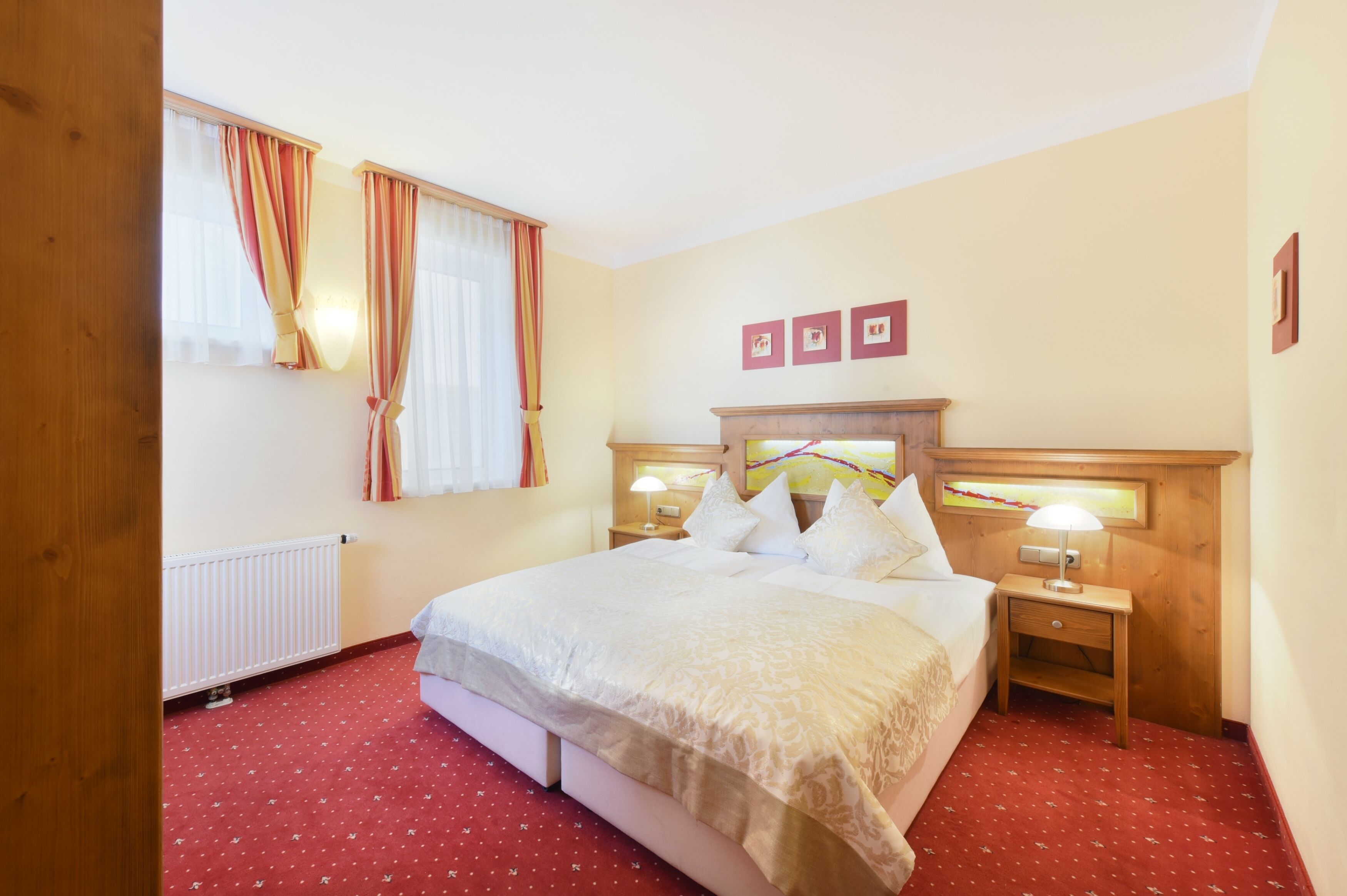 Une chambre d’hôtel avec un grand lit, deux tables de chevet avec des lampes, un radiateur et une fenêtre avec des rideaux.