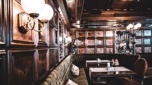 A cozy restaurant interior with wooden paneling, cushioned seating, and table lamps. - Apartmenthaus Hotel Cella Central (Zell am See)