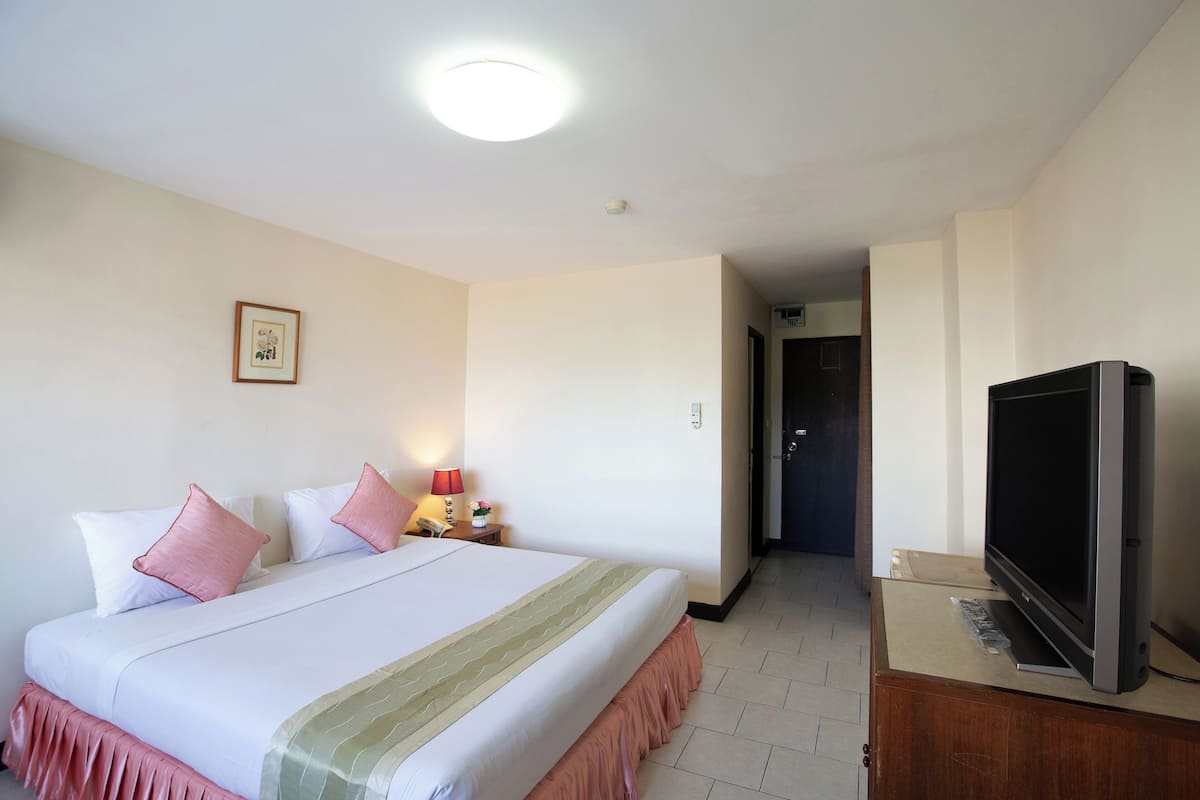 A hotel room with a bed, a television, a nightstand, and a door leading to another room.