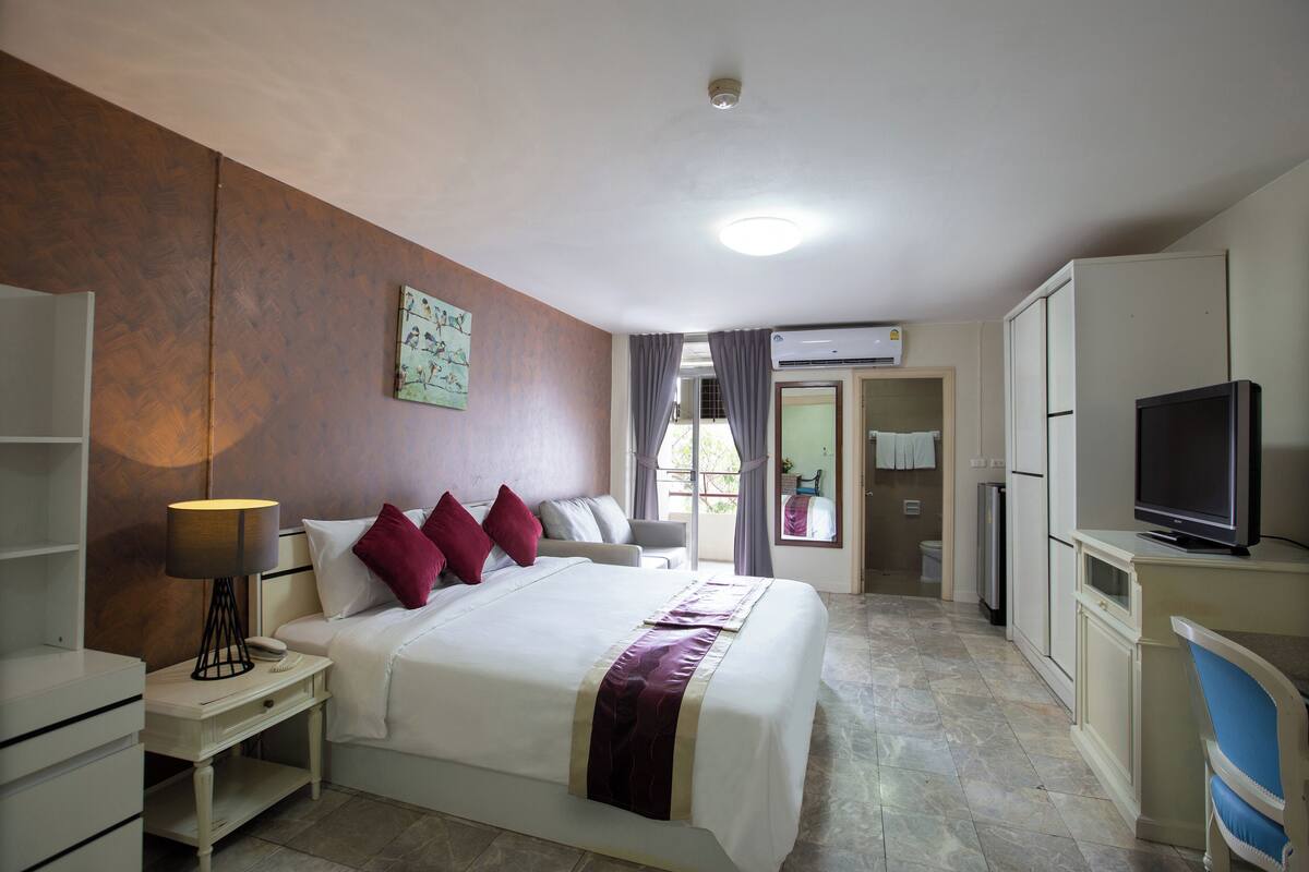 A hotel room with a large bed, a TV, a desk with a lamp, and a wardrobe.