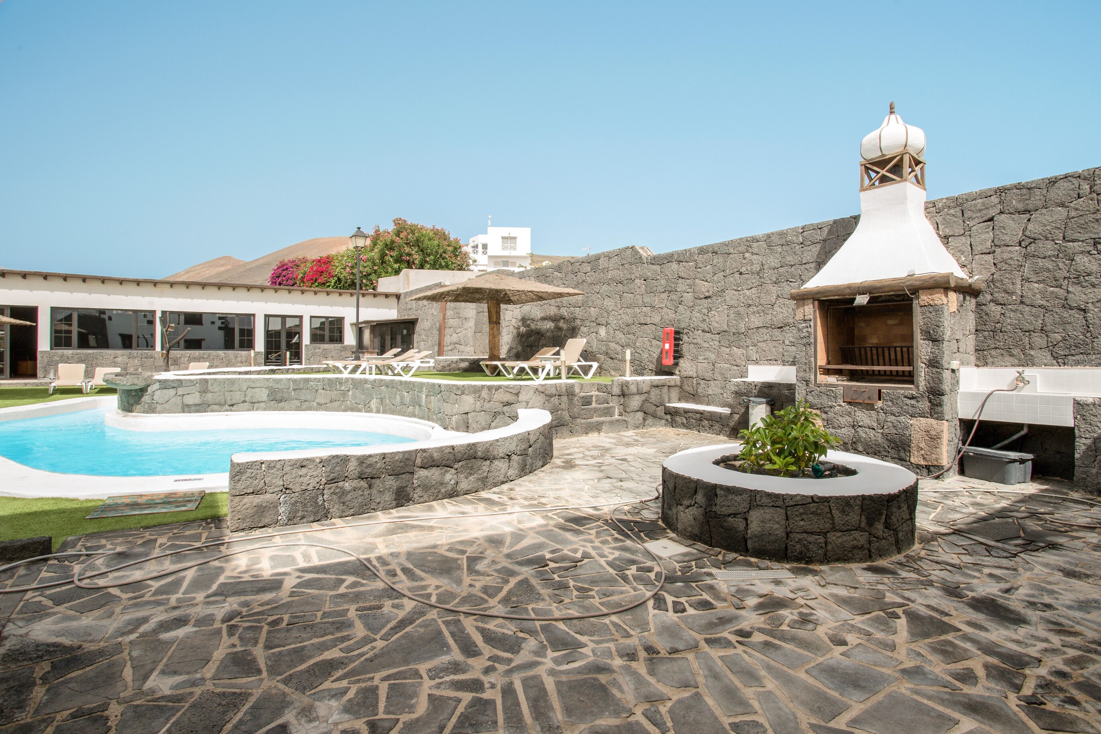 A pool area with lounge chairs, a hot tub, and a stone wall.