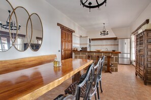 A kitchen with a wooden dining table, chairs, a chandelier, and a refrigerator.