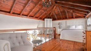 Ein Schlafzimmer mit Holzbalkendecke, einem Bett, einem Nachttisch, einer Kommode, einem Stuhl und einem Balkon mit Geländer.