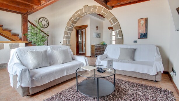 Ein Wohnzimmer mit zwei weißen Sofas, einem runden Couchtisch, einem Steinkleidungsbogen, einer Holzbalkendecke und einer Uhr an der Wand.
