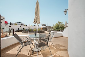 A patio with a table and chairs, a car parked nearby, and a white wall with a lamp.
