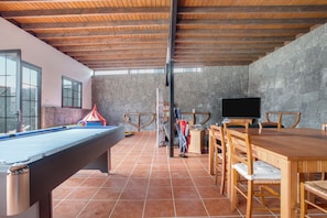 A pool table, wooden dining table, chairs, a television, and a stone wall.