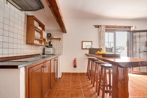 A kitchen with wooden cabinets, a tiled backsplash, a bar area with stools, and a window with a view. - Cosy Apartment "3" with Terrace, Community Pool & Wi-Fi (La Asomada)