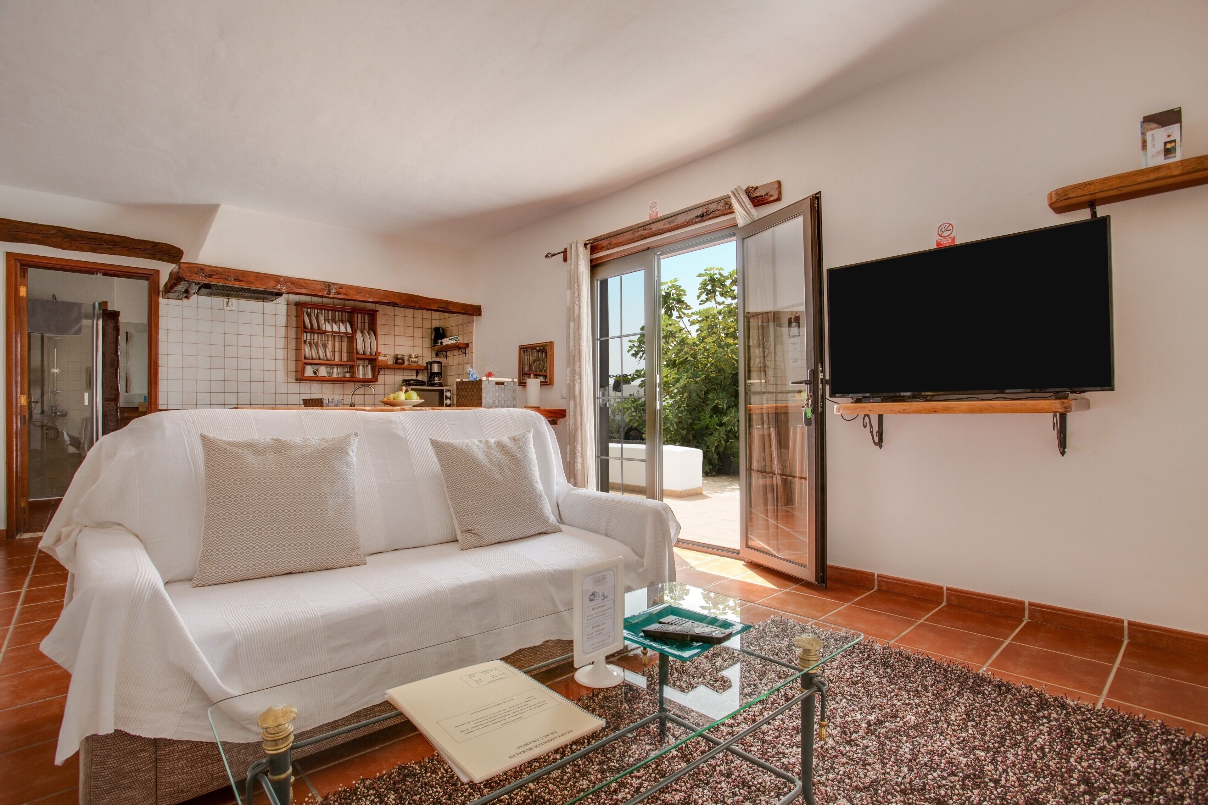 A living room with a white sofa, a glass coffee table, a flat-screen TV, and a sliding glass door leading to a patio.