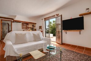 A living room with a white sofa, a glass coffee table, a flat-screen TV, and a sliding glass door leading to a patio. - Cosy Apartment "3" with Terrace, Community Pool & Wi-Fi (La Asomada)