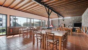 Uma sala de jantar ampla com mesas e cadeiras de madeira, janelas grandes e uma parede de pedra.
