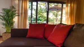 A sectional sofa with red cushions, a potted plant, and a view through large windows. - JOIVY Graca Luminous 2-BR Apartment w/Terrace (Lisboa)