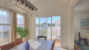 A dining area with a table, chairs, a vase with a plant, and a view through a glass door to the outside. - Pet Friendly (~20lb), 4 BD Townhome, 10 Min to Beach, Near Pool, Tennis, Kayak, and Free Activities! (Millville)