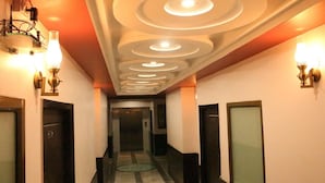 Un pasillo de hotel con un diseño moderno en el techo, varias puertas y luces fijadas a la pared.
