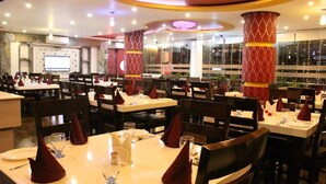 Un restaurante con varias mesas dispuestas para comer, cada una con servilleta roja, cristalería y cubiertos.