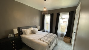 A bedroom with a bed, bedside table, lamp, and a view of the outside through a window. - Entire Apartment walking distance to Cincy River front and COV Wedding Venues (Covington)