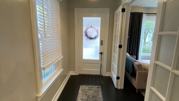 A hallway with a dark floor, white walls, a frosted glass door with a wreath, and a ceiling light. - Entire Apartment walking distance to Cincy River front and COV Wedding Venues (Covington)