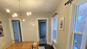 A dining area with a wooden table and chairs, a patterned rug, and large windows with curtains. - Entire Apartment walking distance to Cincy River front and COV Wedding Venues (Covington)
